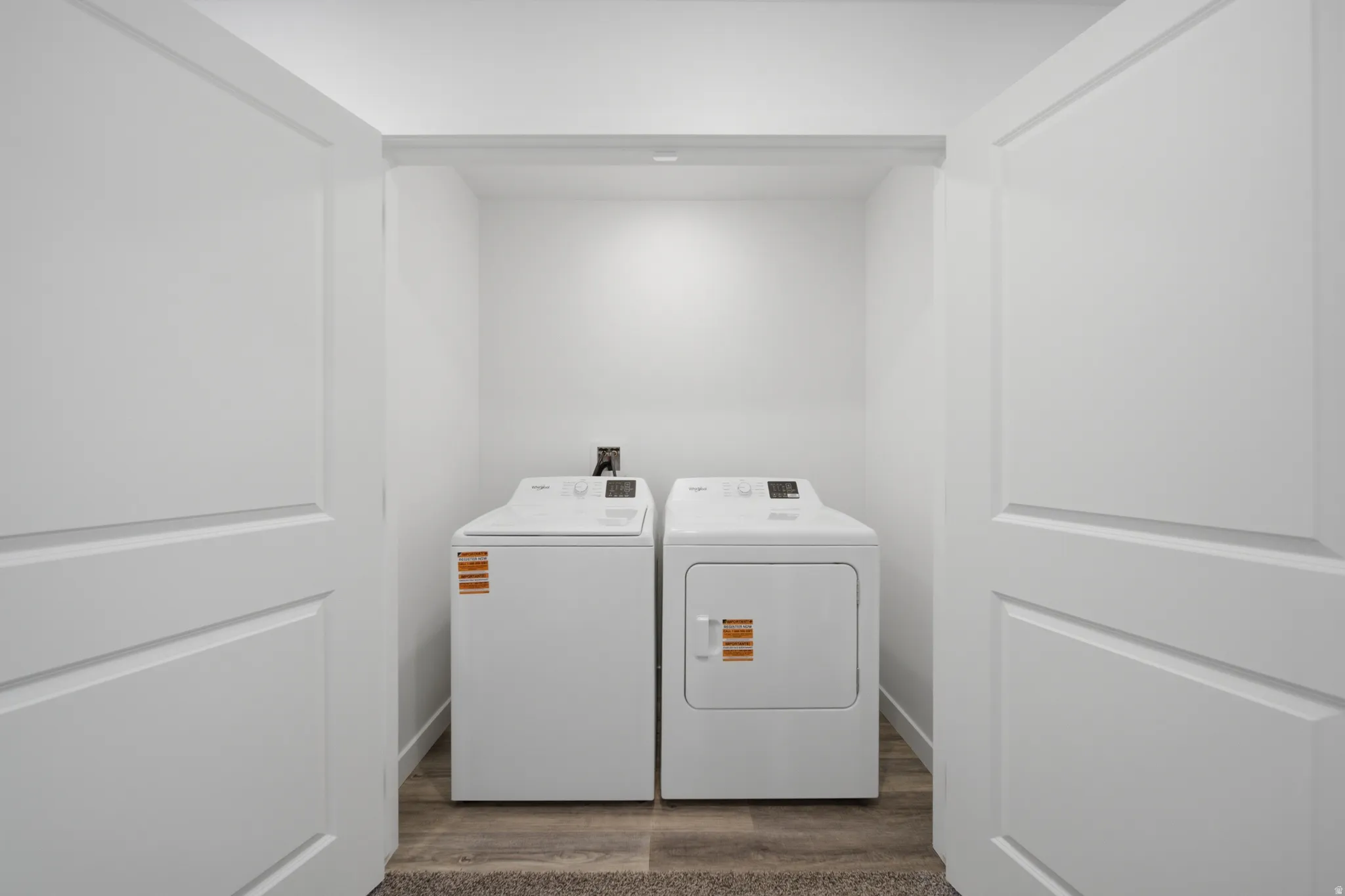 Integrated laundry area with a top-load washer and dryer, featuring wood-finish flooring and bright white walls
