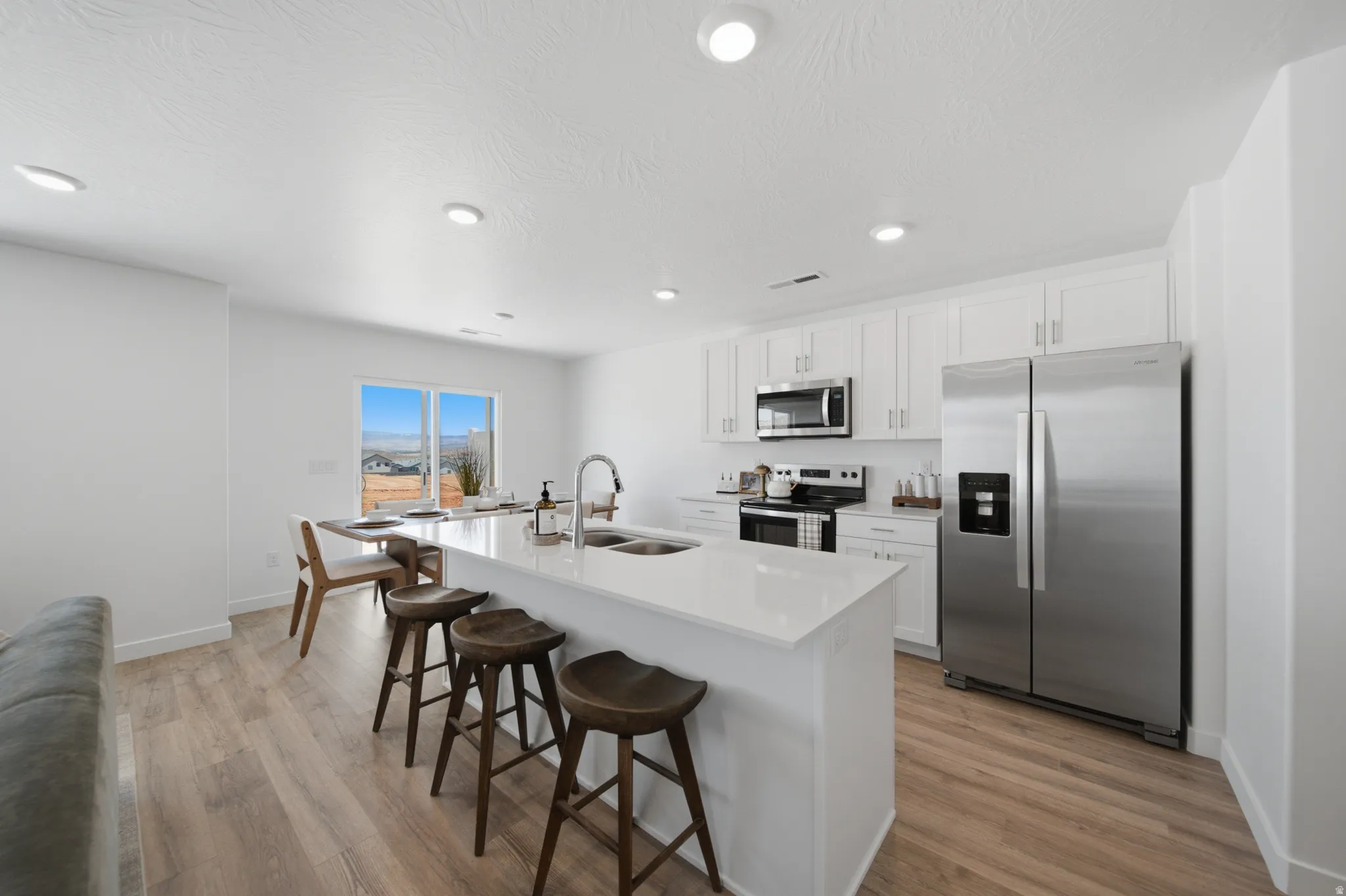 Contemporary kitchen featuring white cabinetry, stainless steel appliances, wood-finish flooring, recessed lighting, and a kitchen island with an integrated sink