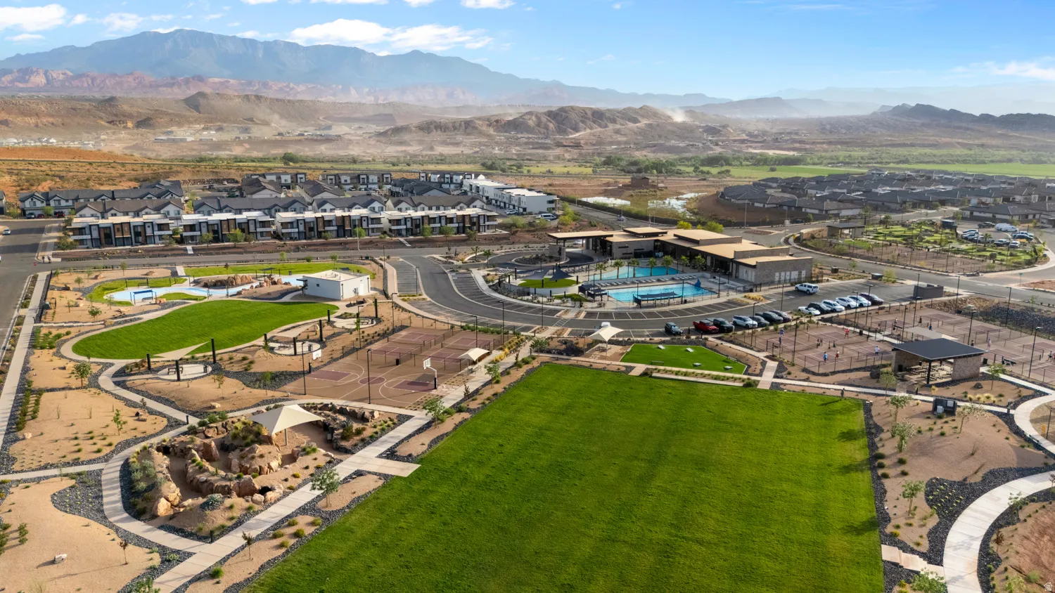 Expansive community grounds featuring a large green space, a multi-use court, and a clubhouse with an outdoor pool