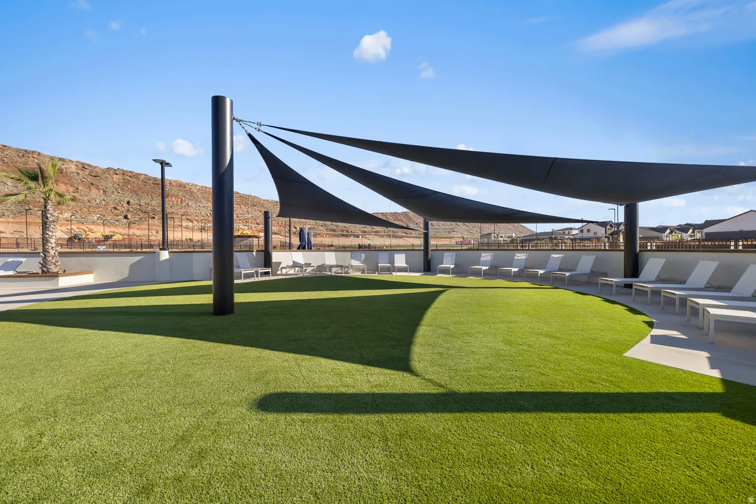 Expansive artificial turf area with multiple shade structures, surrounded by concrete hardscaping