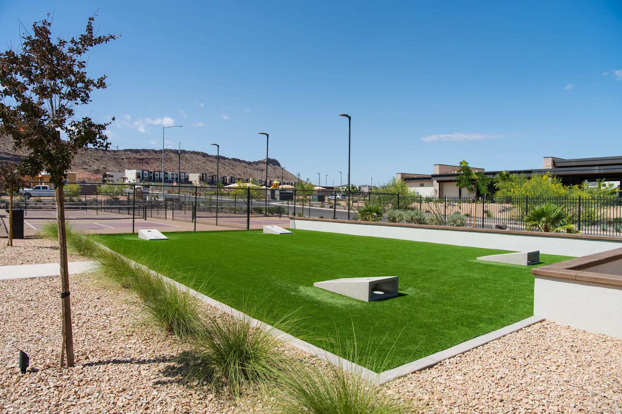 Recreational green space featuring artificial turf, a paved border, and built-in concrete seating