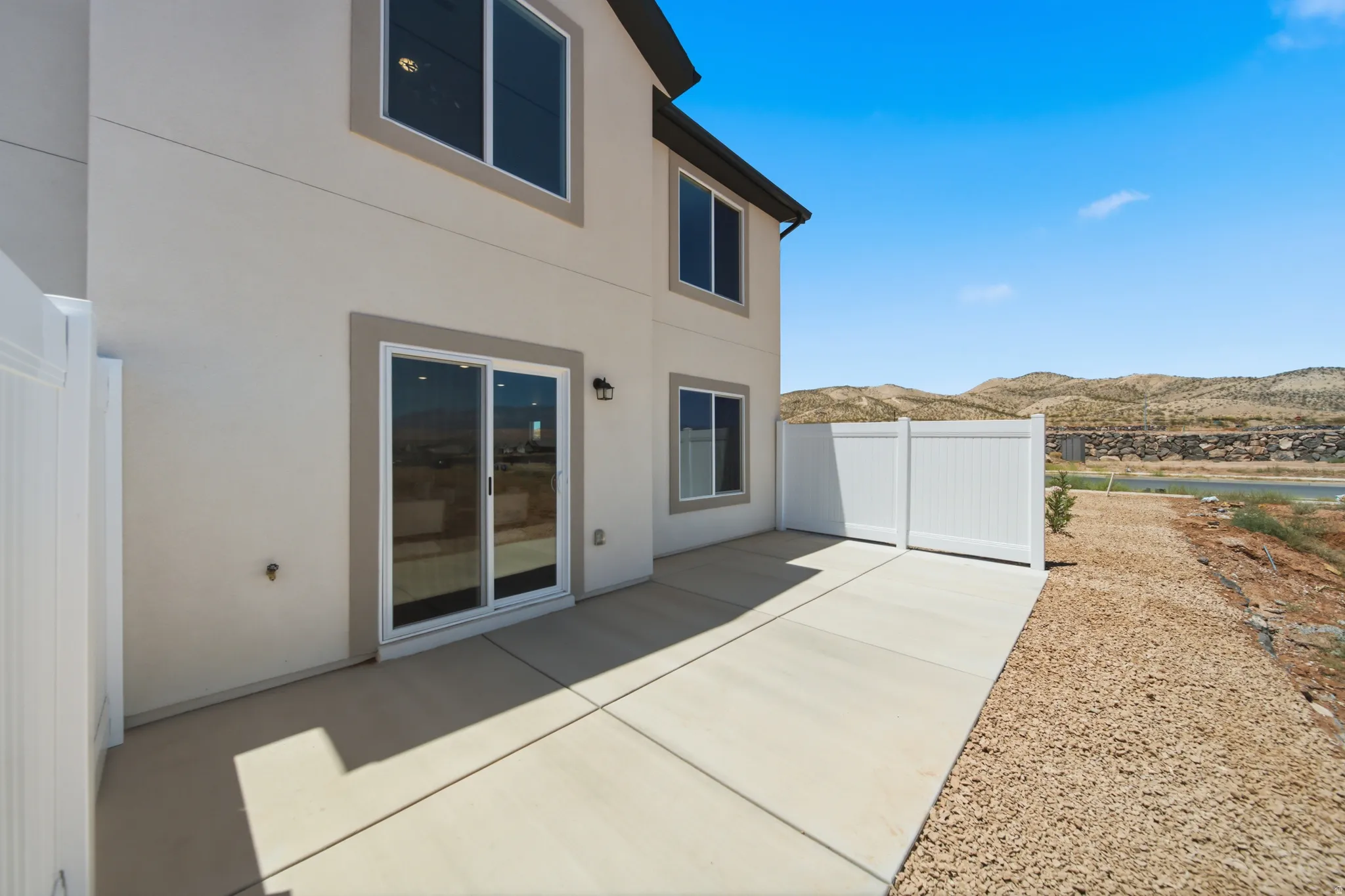 Exterior patio featuring concrete paving, sliding glass door access to the interior, and a white vinyl privacy fence