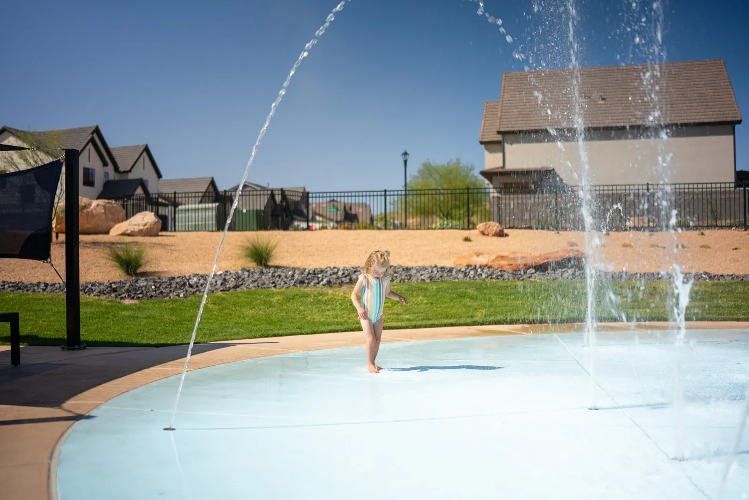 Backyard oasis featuring a splash pad with multiple water jets, expansive lawn, decorative stone landscaping, and multi-level hardscaping