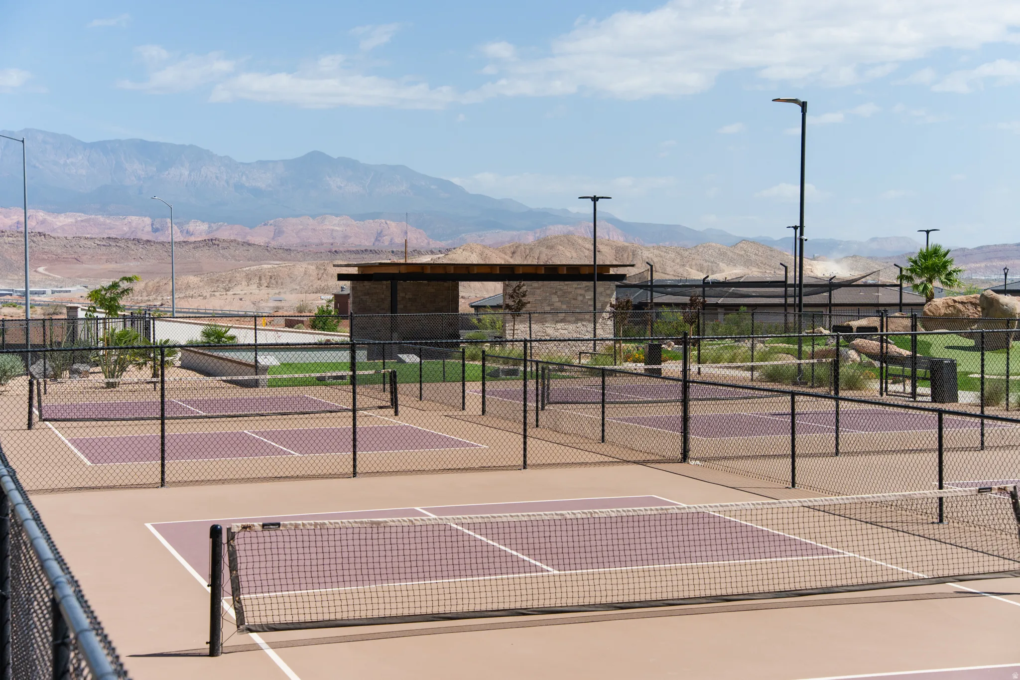 Professional tennis court complex featuring multiple clay courts with regulation net systems, sturdy black perimeter fencing, and integrated lighting infrastructure
