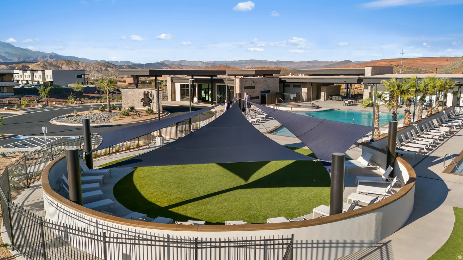 Resort-style resort deck featuring a circular lounge area with artificial turf center, multiple shade structures, lounge seating, and an adjacent resort pool with striped loungers