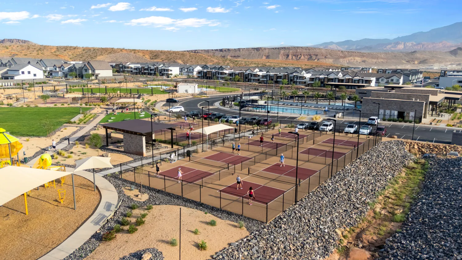 Expansive recreational court complex featuring multiple clay tennis courts with professional-grade netting, manicured turf areas, and integrated shade structures