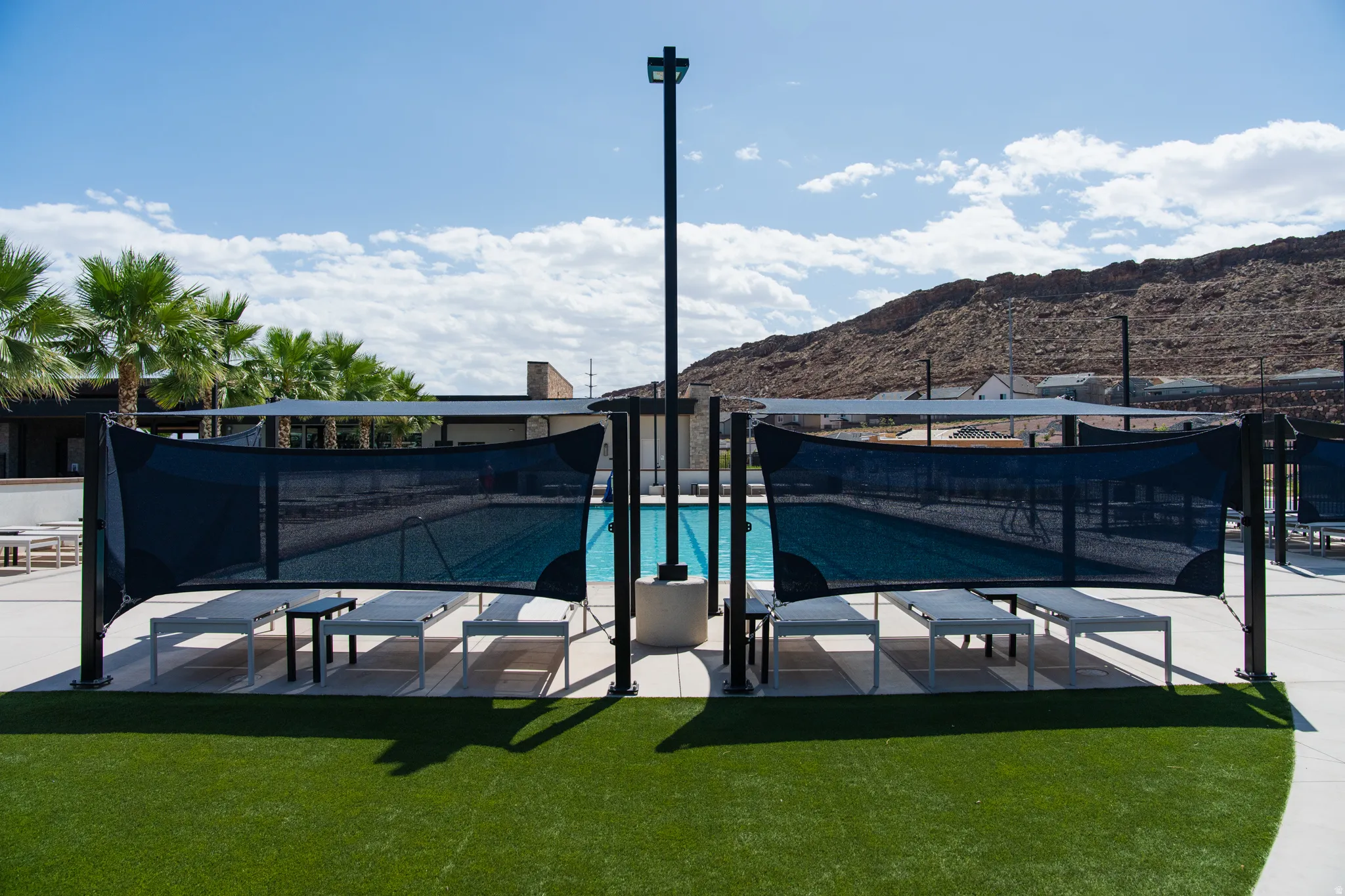 Resort-style pool area featuring a rectangular pool, artificial turf, modern shade structures, and lounge seating
