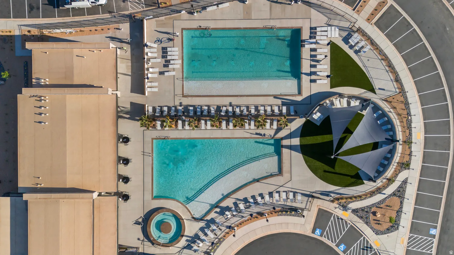 Community pool area featuring two distinct swimming pools, an integrated spa, ample surrounding deck space, and a circular turf lounge area with shade sails