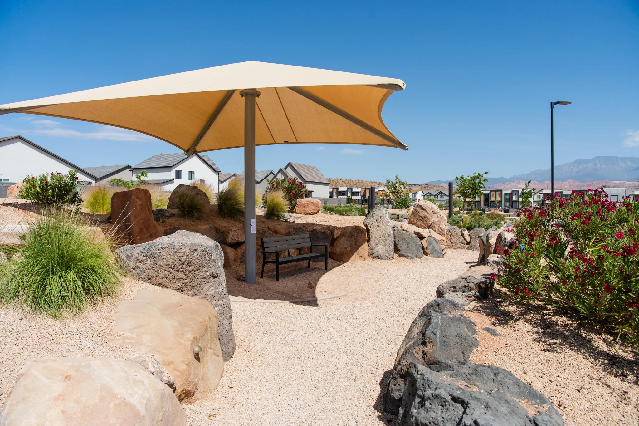 Shade structure with a built-in bench, surrounded by desert landscaping with boulders, gravel pathways, and low-maintenance plantings
