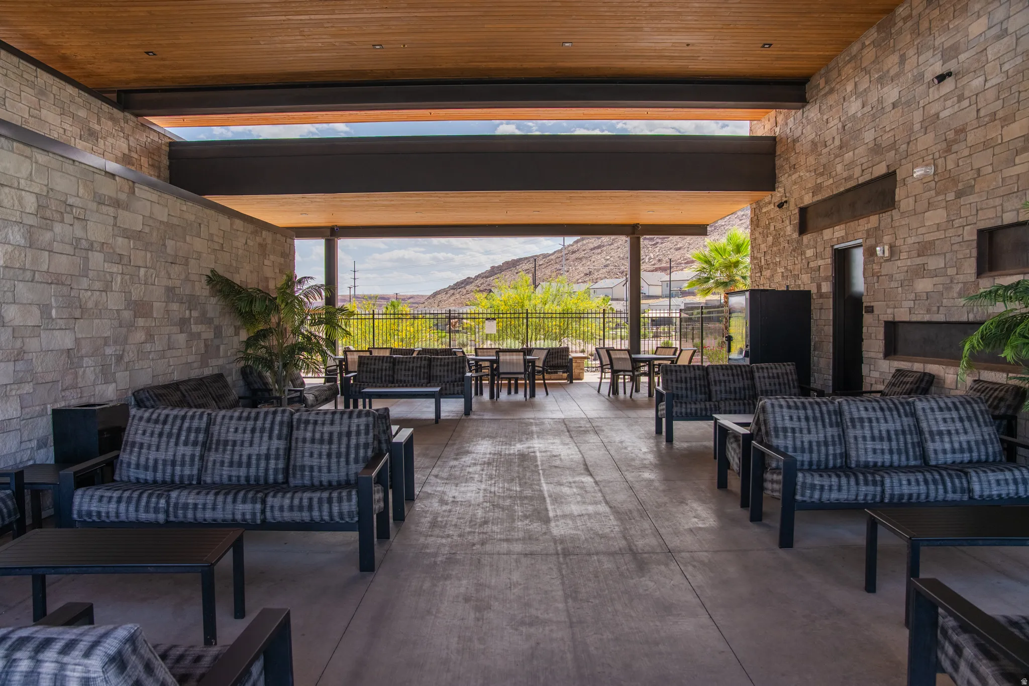 Expansive covered outdoor lounge area featuring stone-clad walls, wood-finish ceiling, exposed structural beams, and a built-in linear fireplace