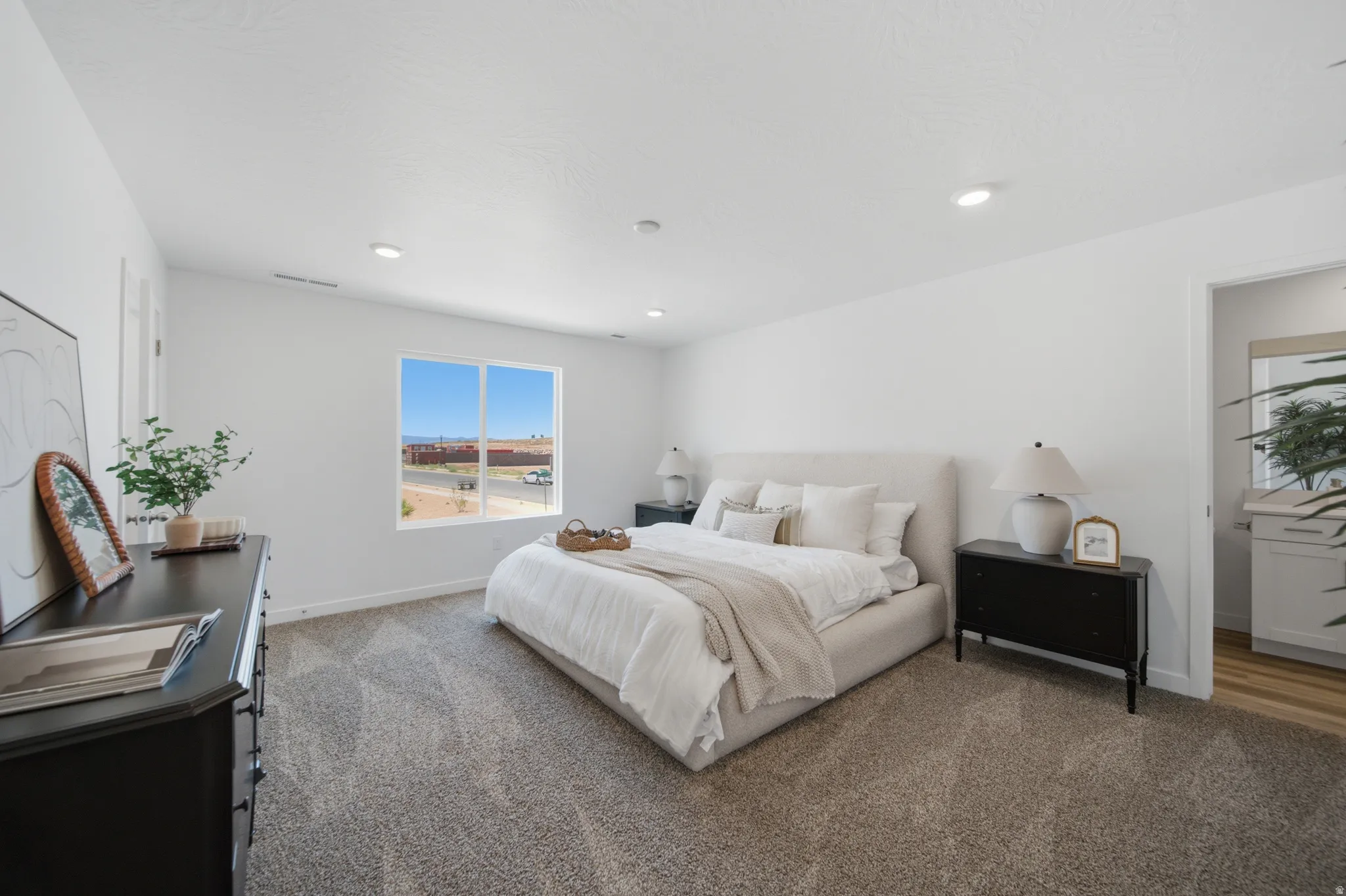 Spacious bedroom with light gray carpet flooring, recessed lighting, and a large window providing ample natural light