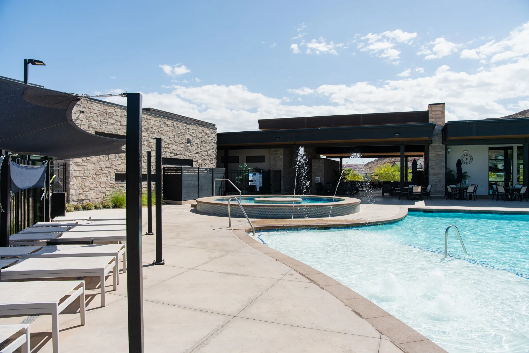 Resort-style pool and spa area featuring crystal-clear water, integrated hot tub with surrounding concrete decking, modern pergola structure with integrated shade elements, and contemporary stone and metal architectural detailing