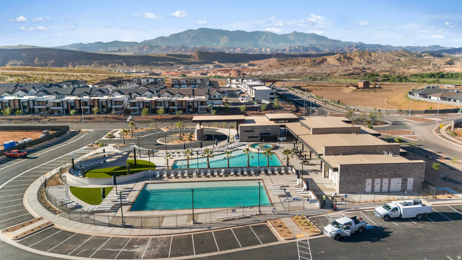 Community amenity center with two swimming pools, expansive paved deck with lounge seating, and a large covered patio