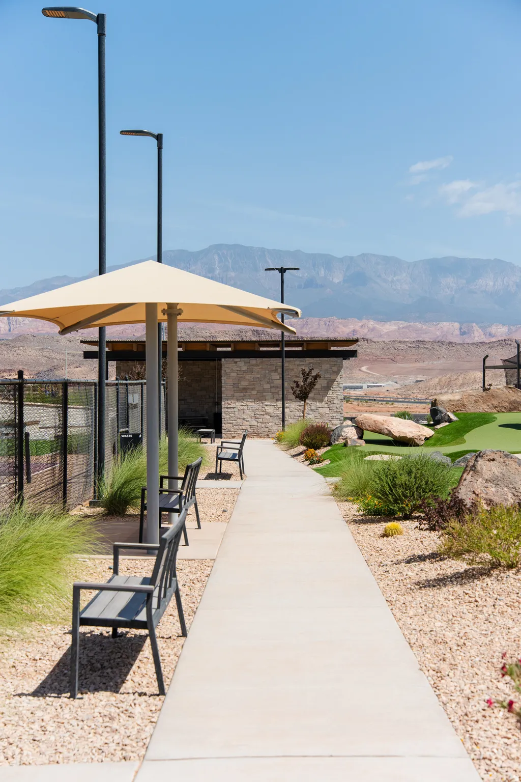 Outdoor walkway with ample seating, featuring a shade umbrella, streetlights, and xeriscape landscaping