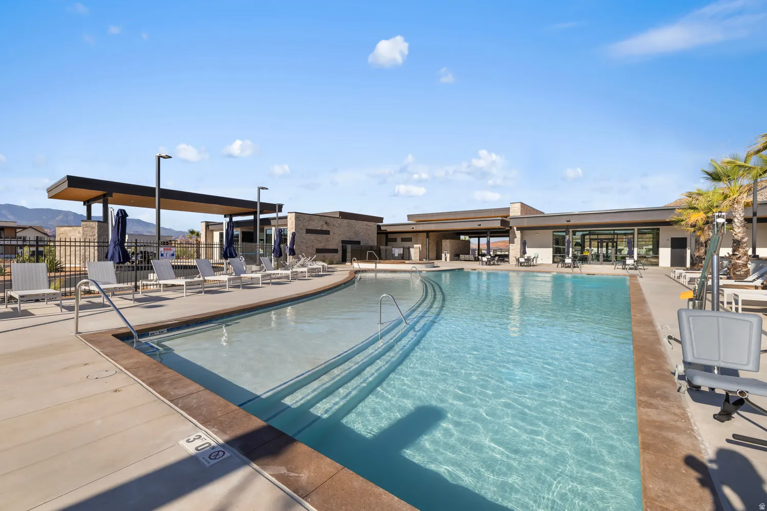 Expansive resort-style swimming pool featuring a shallow entry, integrated lounge seating, and a surrounding paved deck