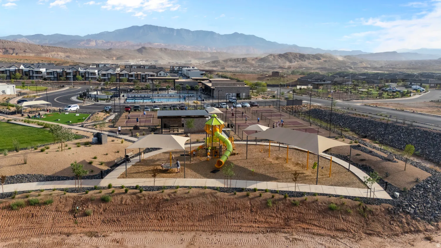 Community amenities featuring a playground, multiple sports courts, a swimming pool, and green spaces, all surrounded by mountainous terrain