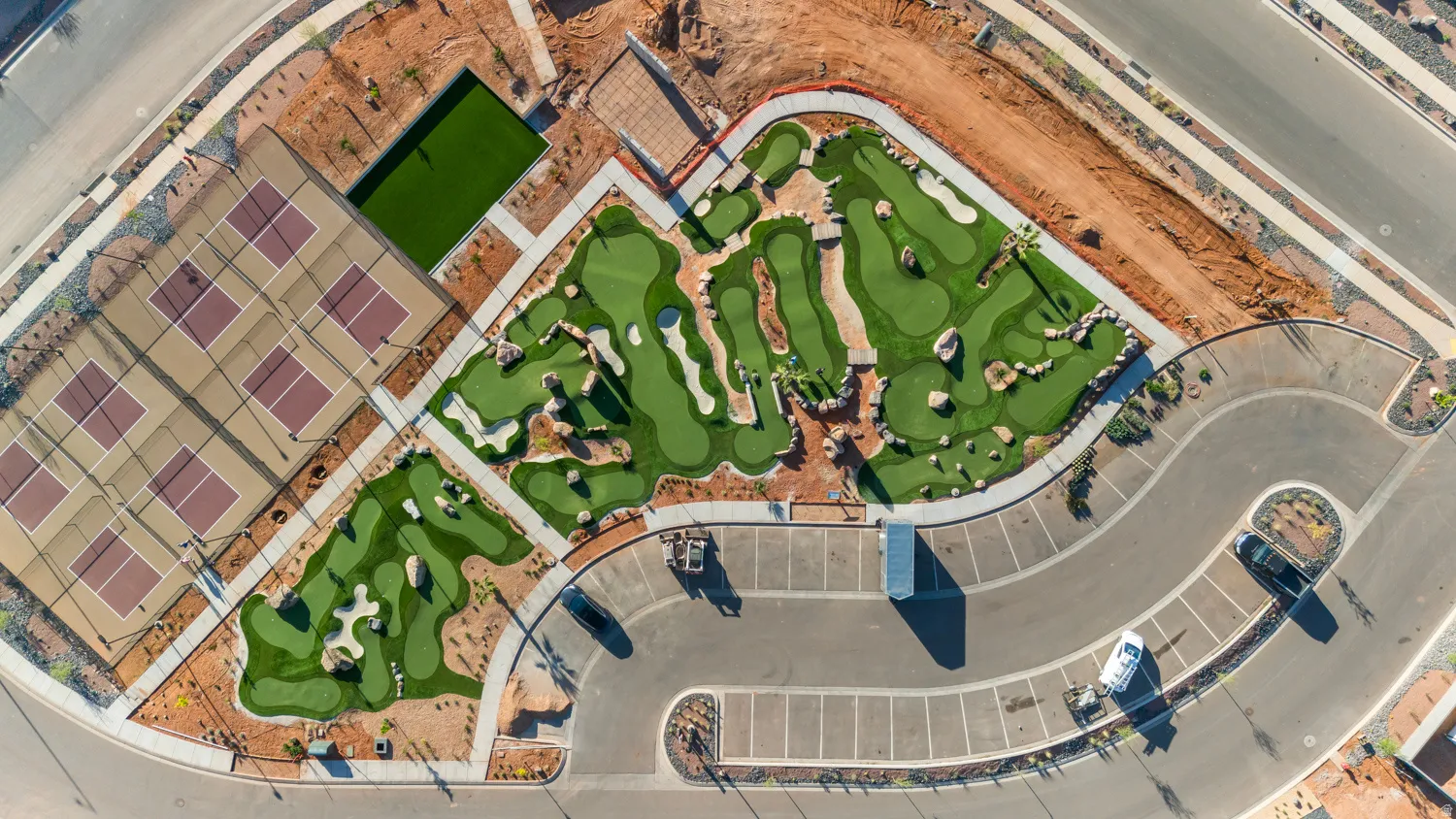 Aerial view showcasing a thoughtfully designed recreational courtyard featuring a professionally landscaped putting green with multiple holes, ample hardscaped parking and circulation areas, mature green spaces, and integrated hardscape pathways