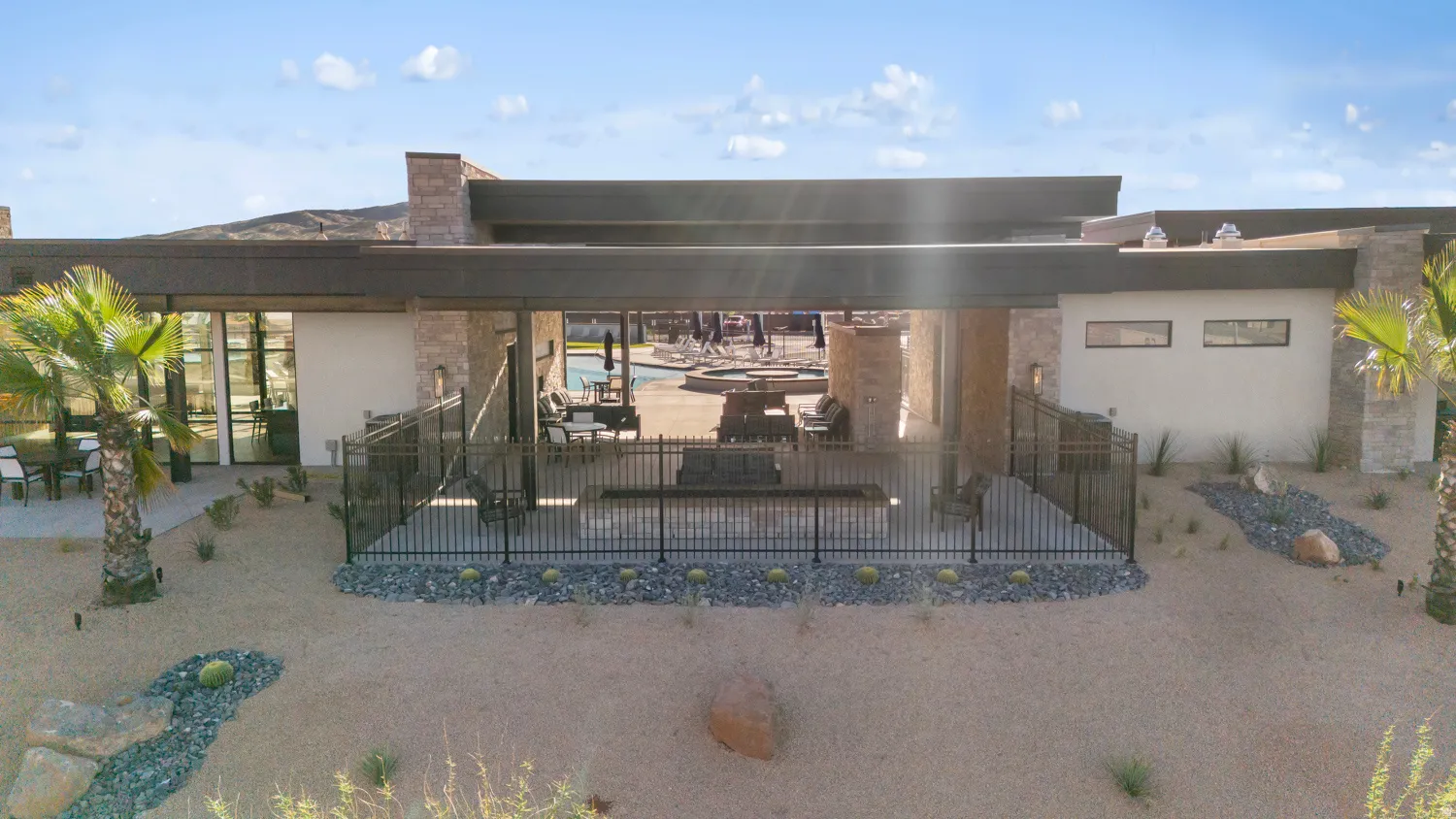 Modern desert residence featuring a covered outdoor entertaining space with integrated shade structure, black metal railings, and direct access to expansive grounds