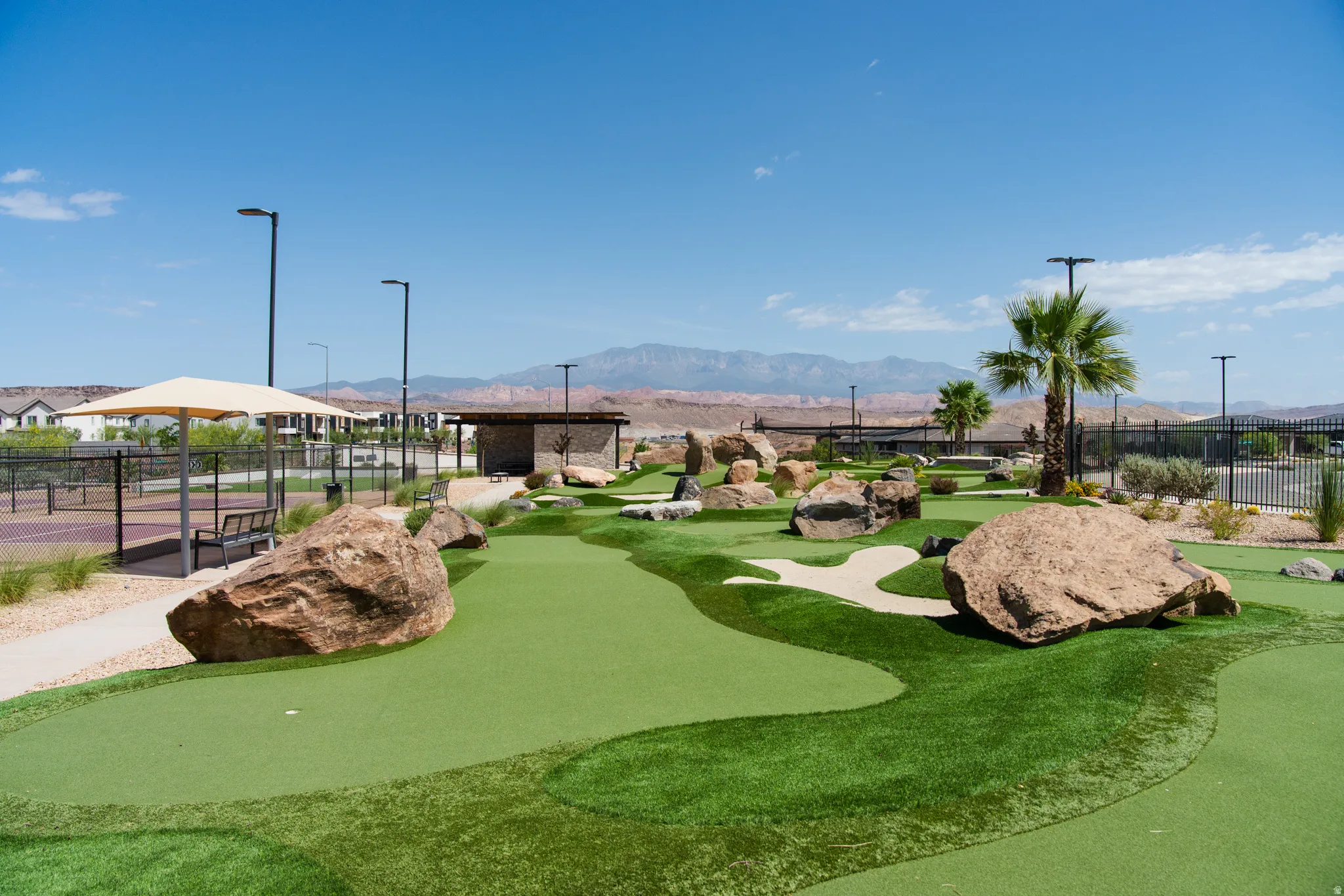 Miniature golf course featuring artificial turf, large rock landscaping, and palm trees