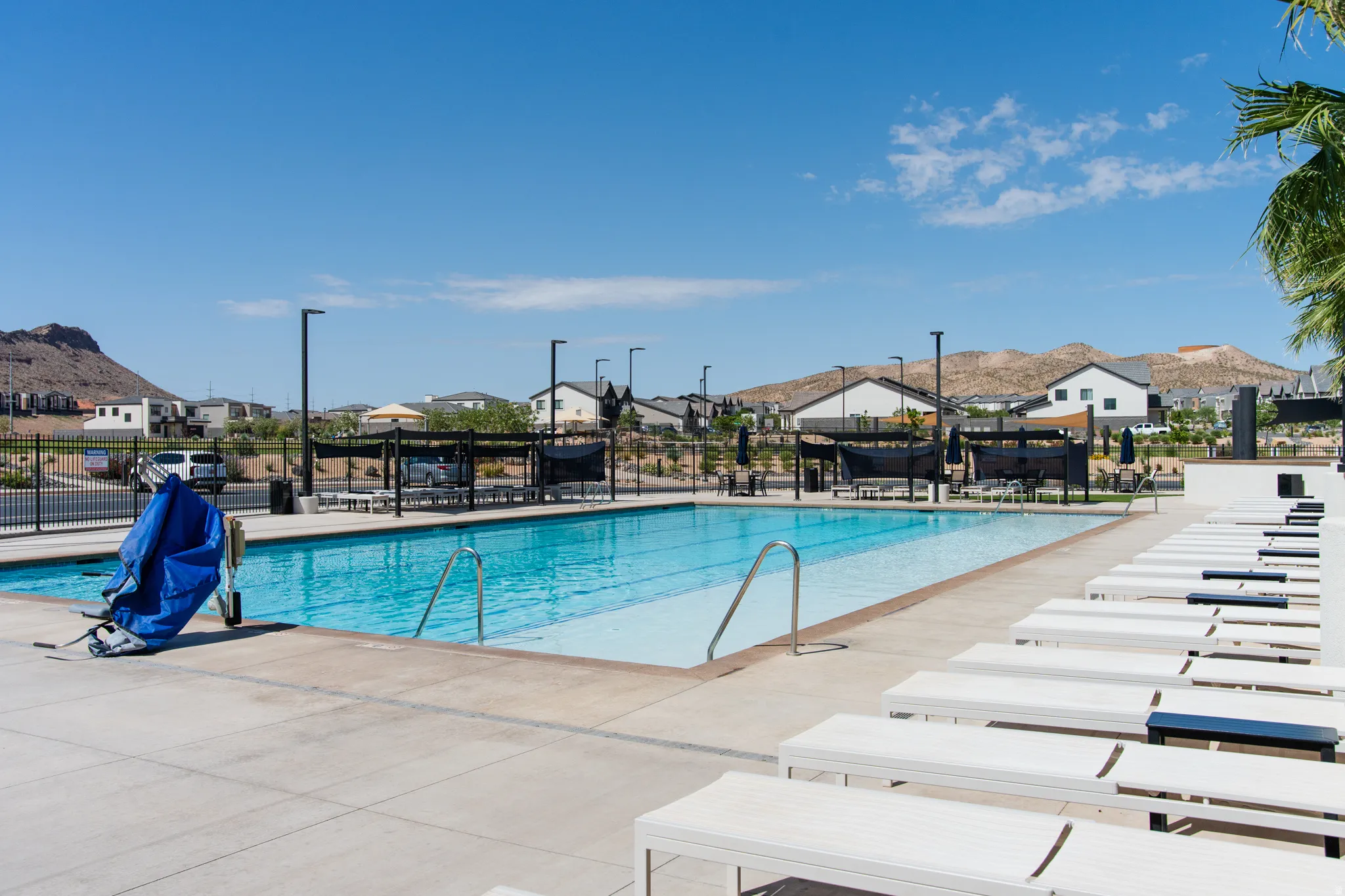 Community swimming pool with surrounding concrete decking, multiple lounge chairs, and shaded seating areas