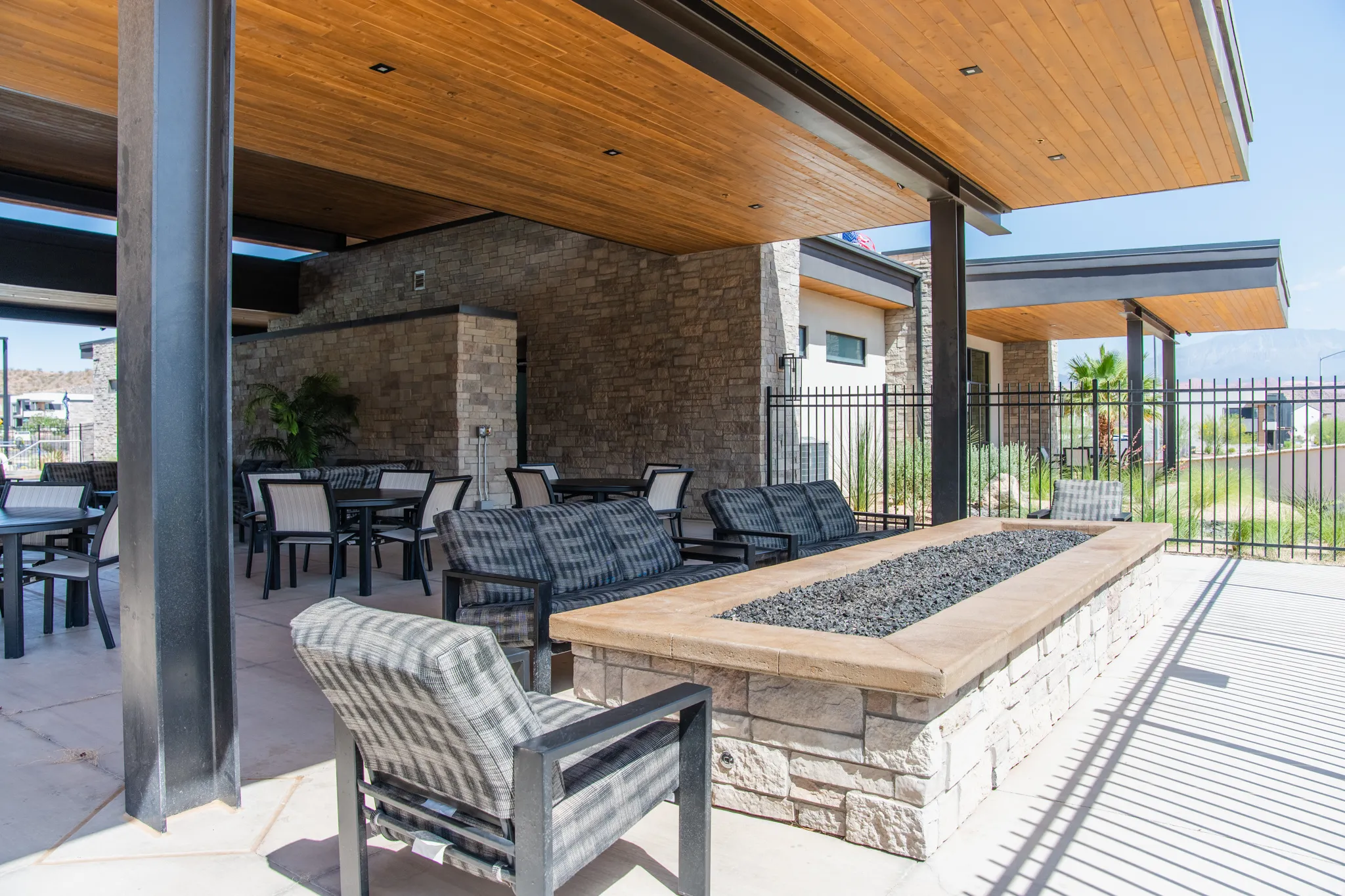 Expansive outdoor patio featuring a stone-clad fire pit, wood-finish ceiling, and exposed structural beams