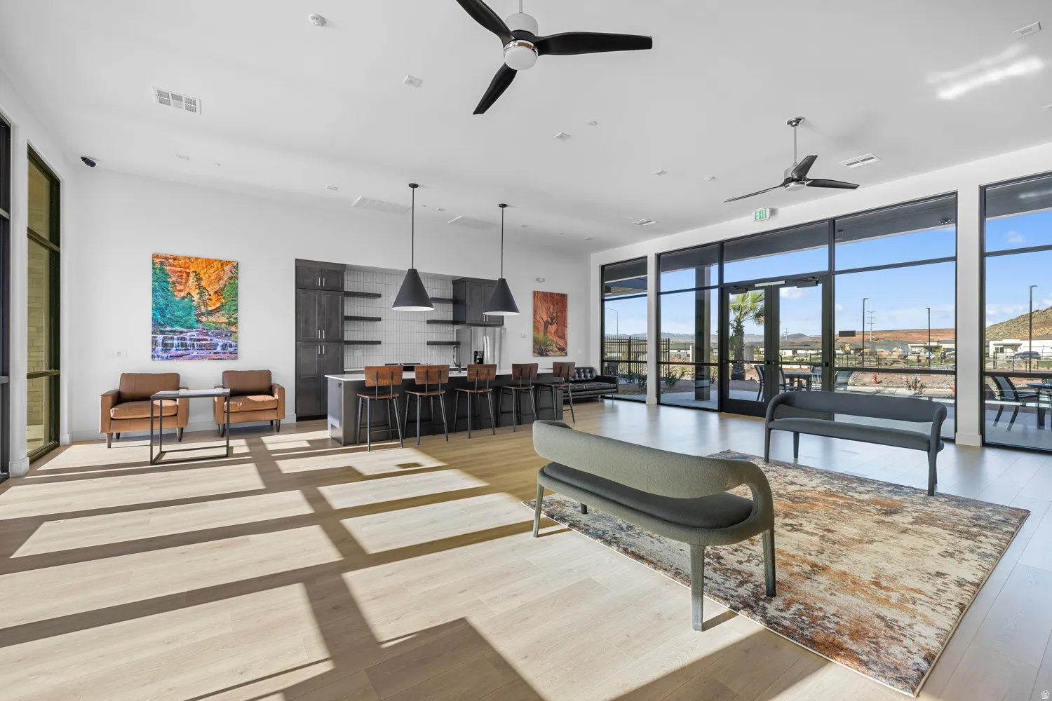 Spacious common area featuring light wood-finish flooring, a full-height window wall, and contemporary ceiling fans