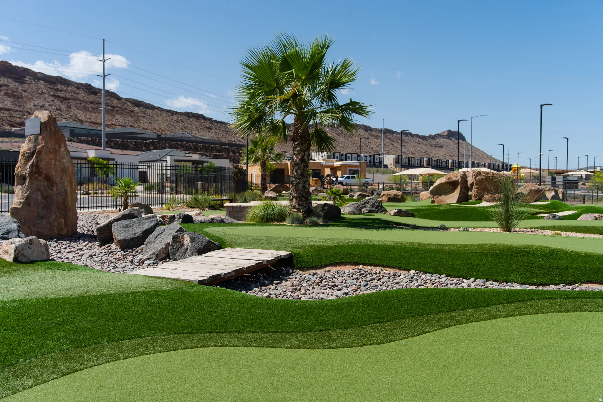 Expansive recreational grounds featuring professionally manicured synthetic turf, mature palm tree landscaping, natural stone outcroppings and boulders, decorative gravel accents, and perimeter lighting throughout the grounds