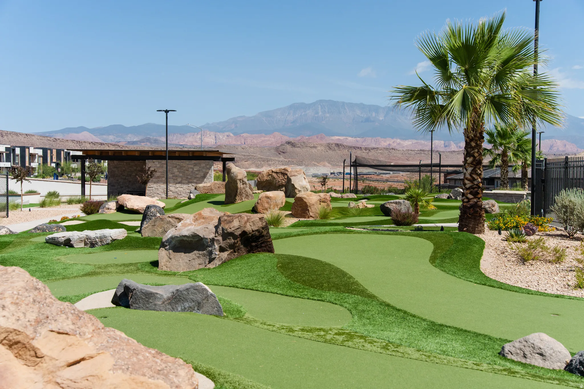 Miniature golf course featuring artificial turf, natural rock landscaping, and mature palm trees
