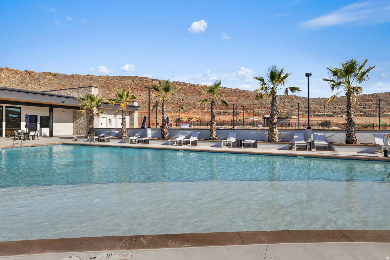 Expansive swimming pool featuring a shallow entry area, surrounded by concrete decking and multiple lounge chairs
