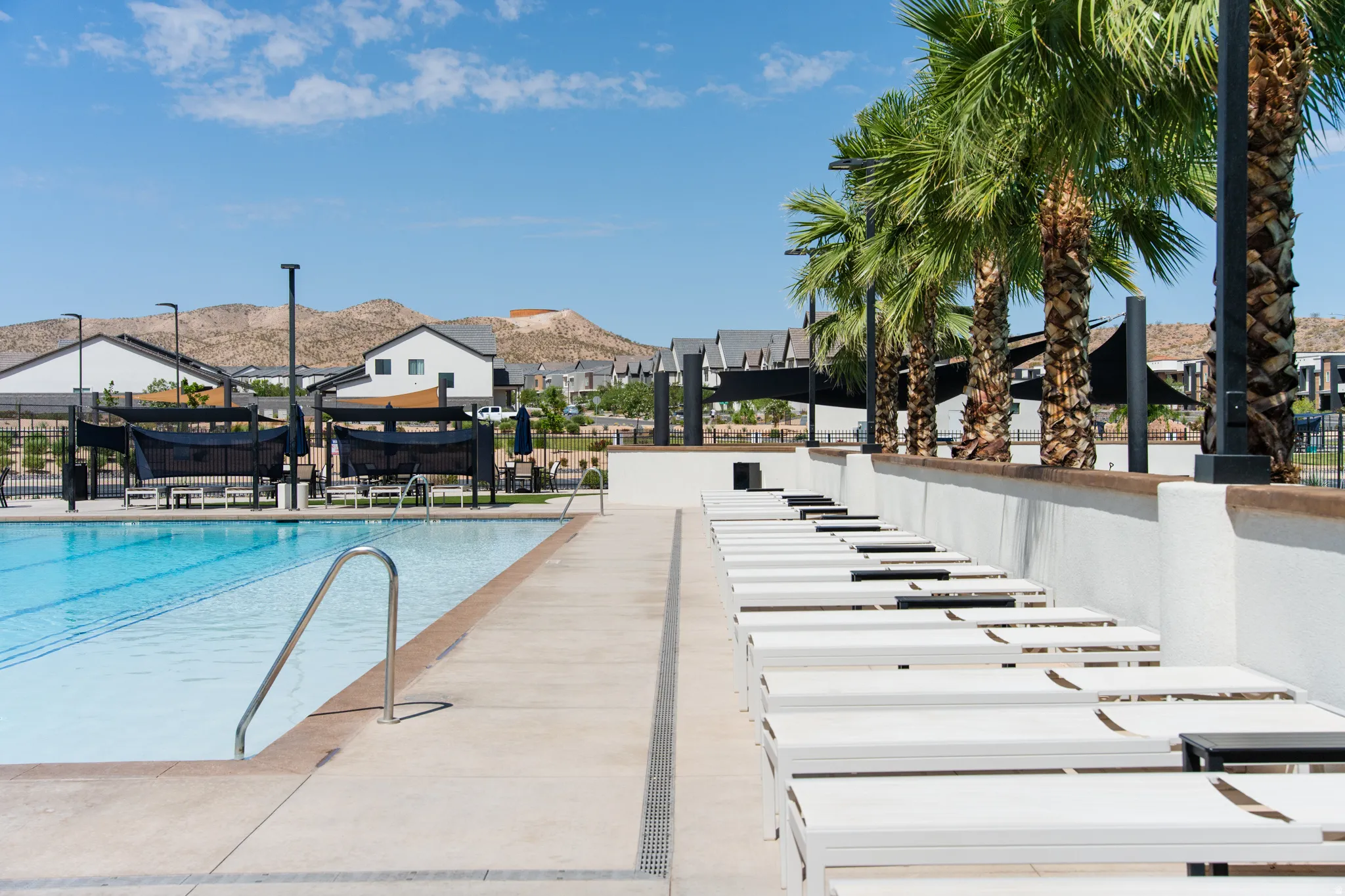 Resort-style pool area featuring crystal-clear waters, integrated spa lounging with black accent detailing, mature palm trees providing natural shade, and expansive hardscaped decking