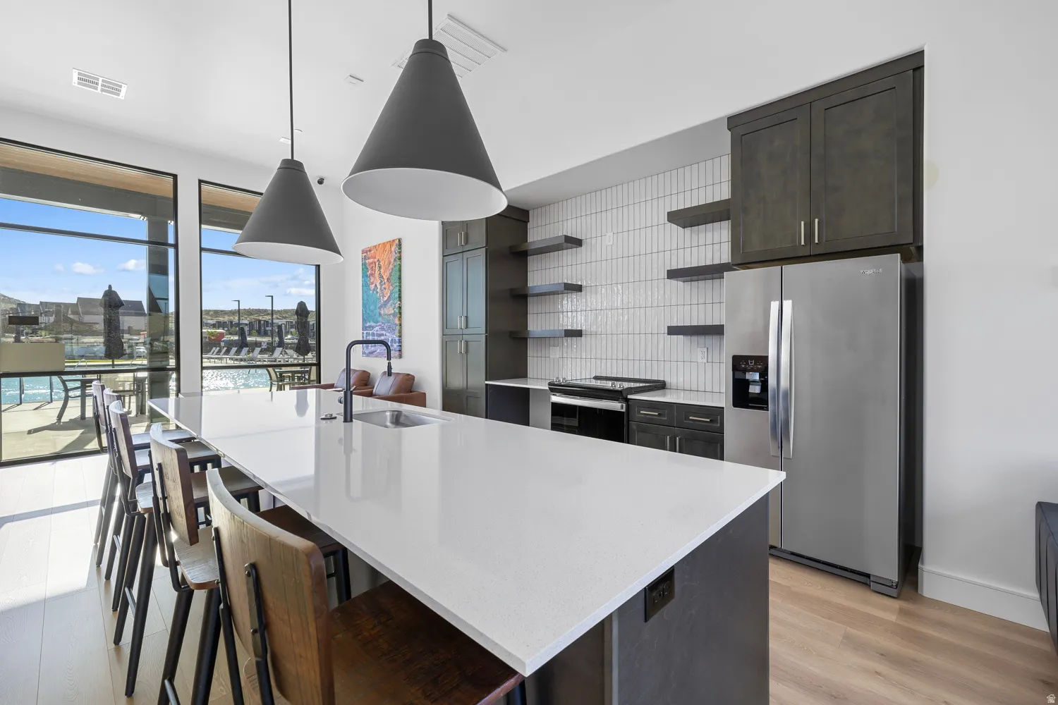 Modern kitchen featuring an expansive island with a built-in sink and seating, contemporary pendant lighting, a full suite of stainless steel appliances, and a tiled backsplash with open shelving