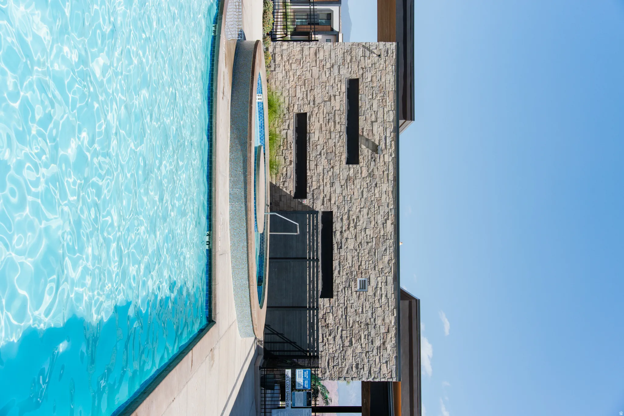 Resort-style swimming pool with an integrated spa, complemented by a stone-clad building featuring modern architectural elements and privacy screening