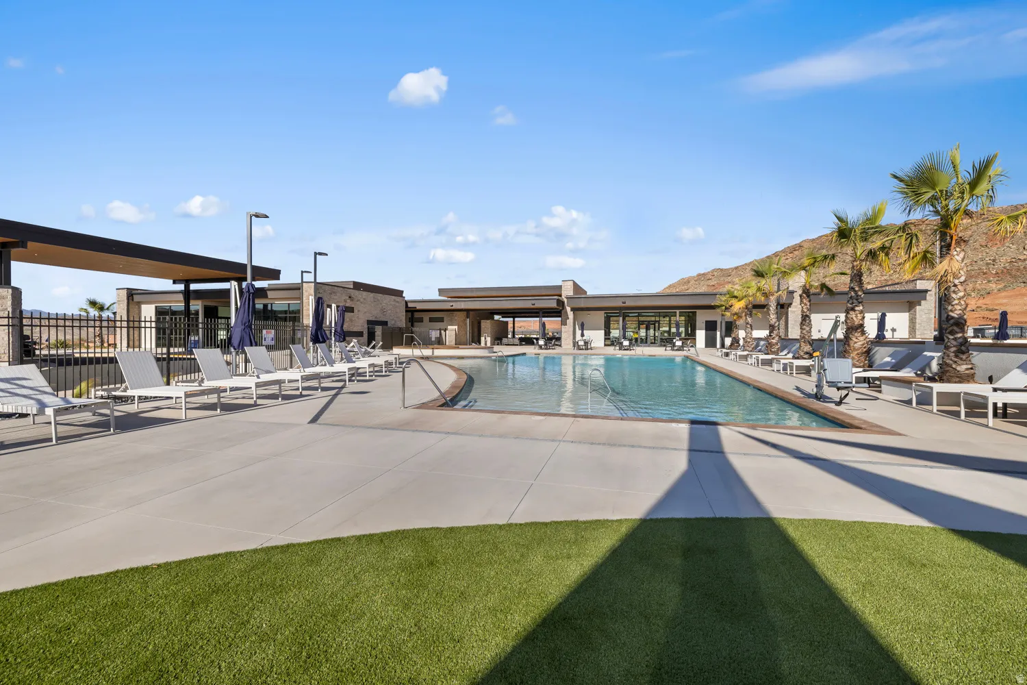 Expansive swimming pool with concrete decking, surrounding lounge areas, artificial turf accents, and desert mountain backdrop