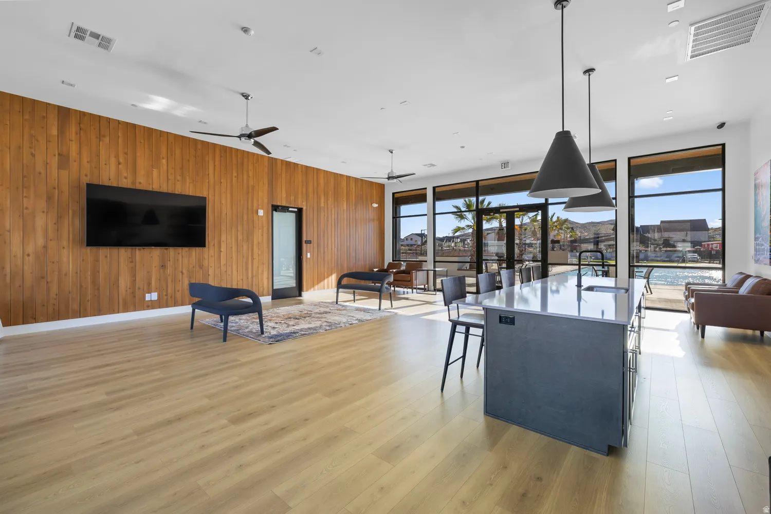 Spacious open area featuring floor-to-ceiling windows, waterfront views, wood-finish flooring, and a large central island with seating