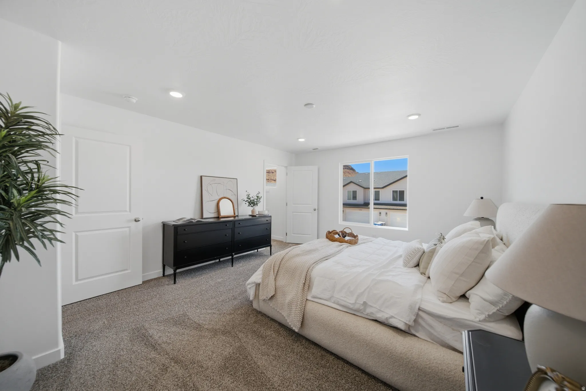 Spacious bedroom with light gray carpet flooring, recessed lighting, white walls, a large window, and a white paneled door