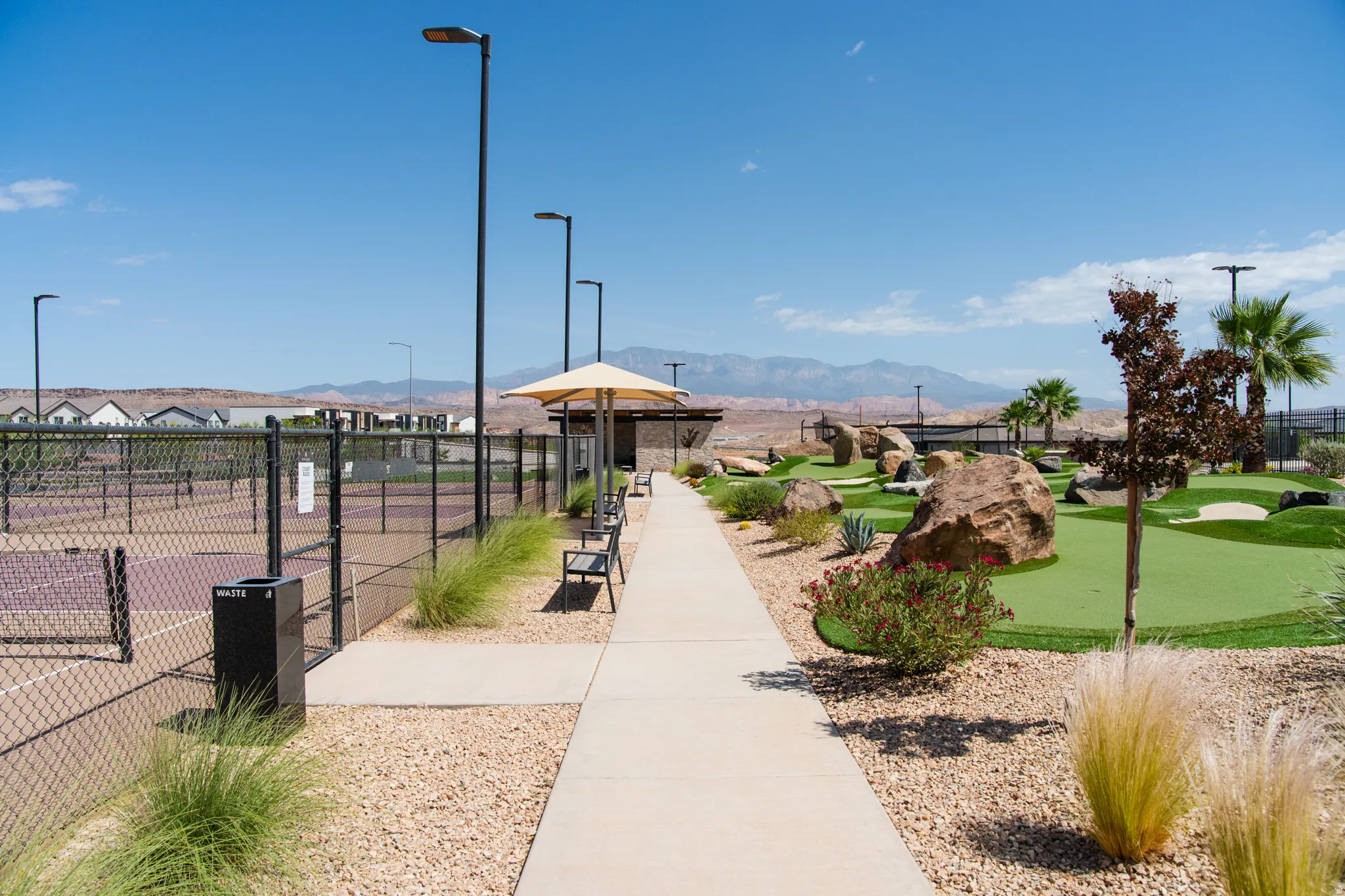 Outdoor recreation area featuring a paved walkway, tennis courts, a putting green, and desert landscaping