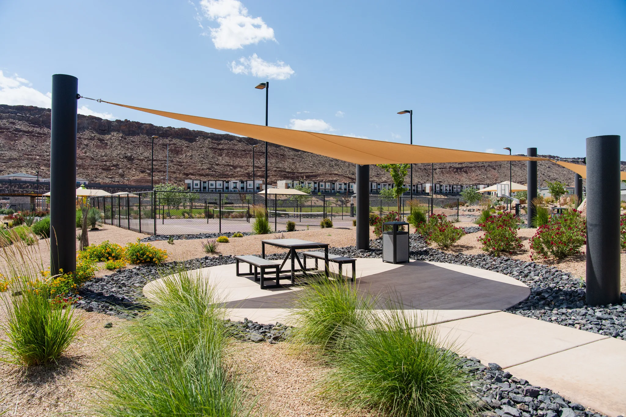 Outdoor amenity space featuring a large shade sail structure, concrete pathways, and desert landscaping