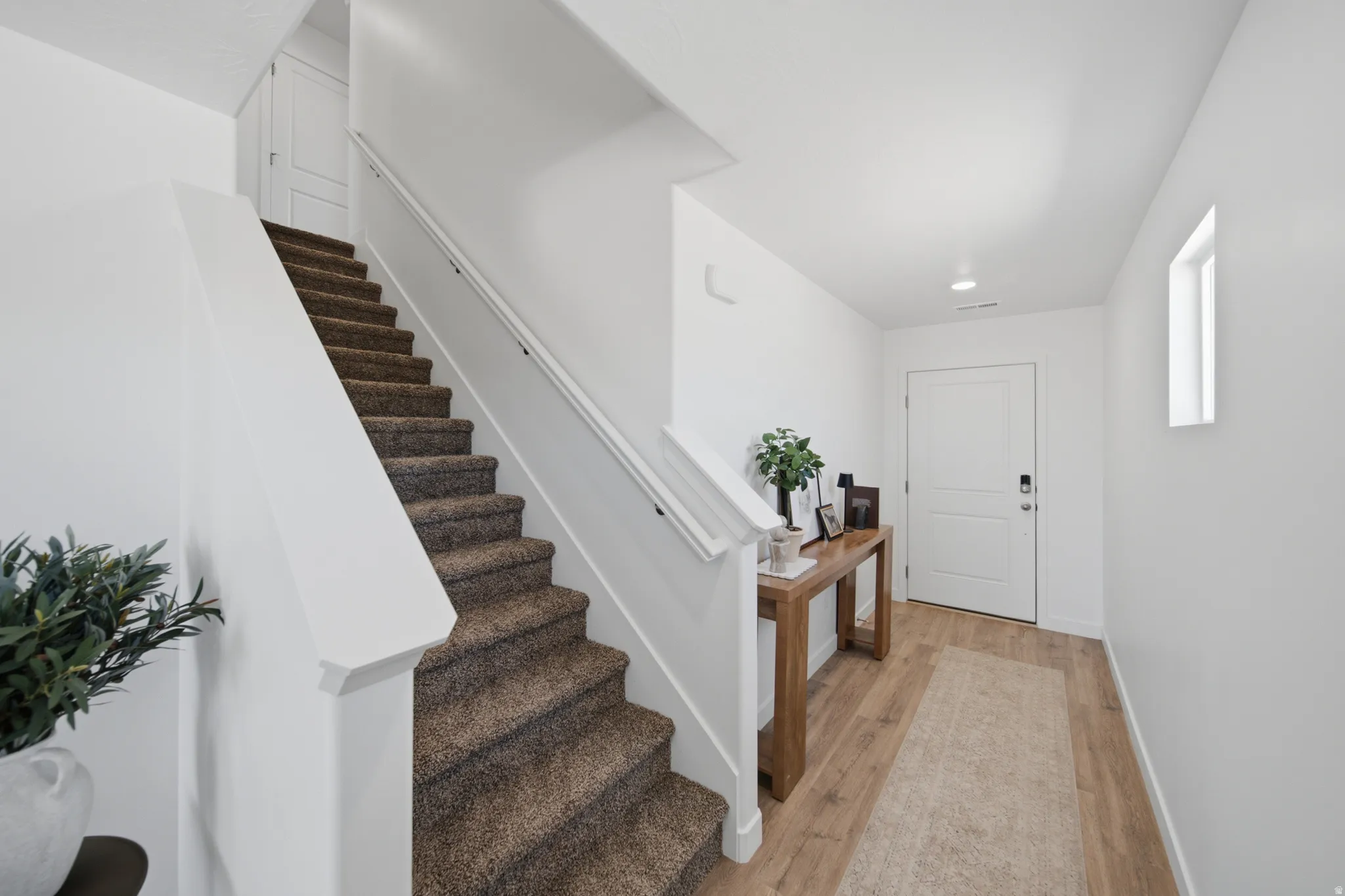 Entryway featuring wood-finish flooring, a carpeted staircase, and abundant natural light from a rectangular window