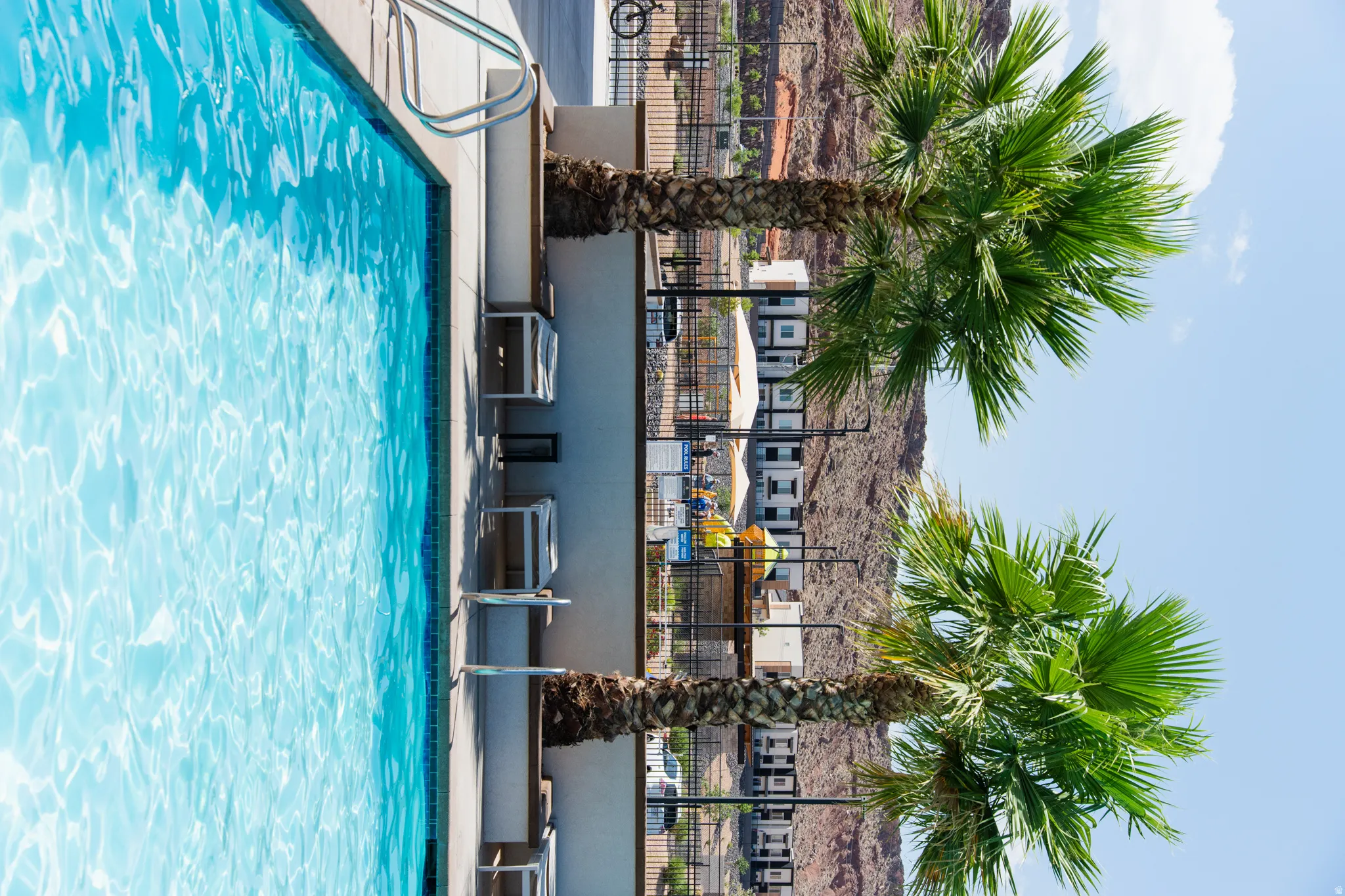 Resort-style swimming pool featuring crystal-clear turquoise water, modern pool deck with integrated lounging areas, and mature palm trees providing natural shade