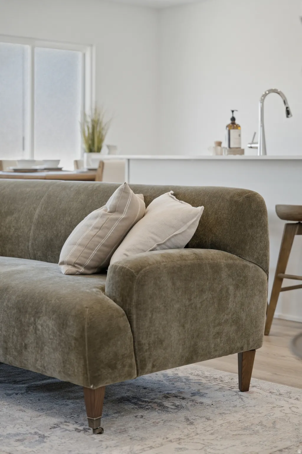 Contemporary living room featuring a curved upholstered sofa in neutral linen-blend fabric with tapered wood legs and casters, complemented by coordinating throw pillows