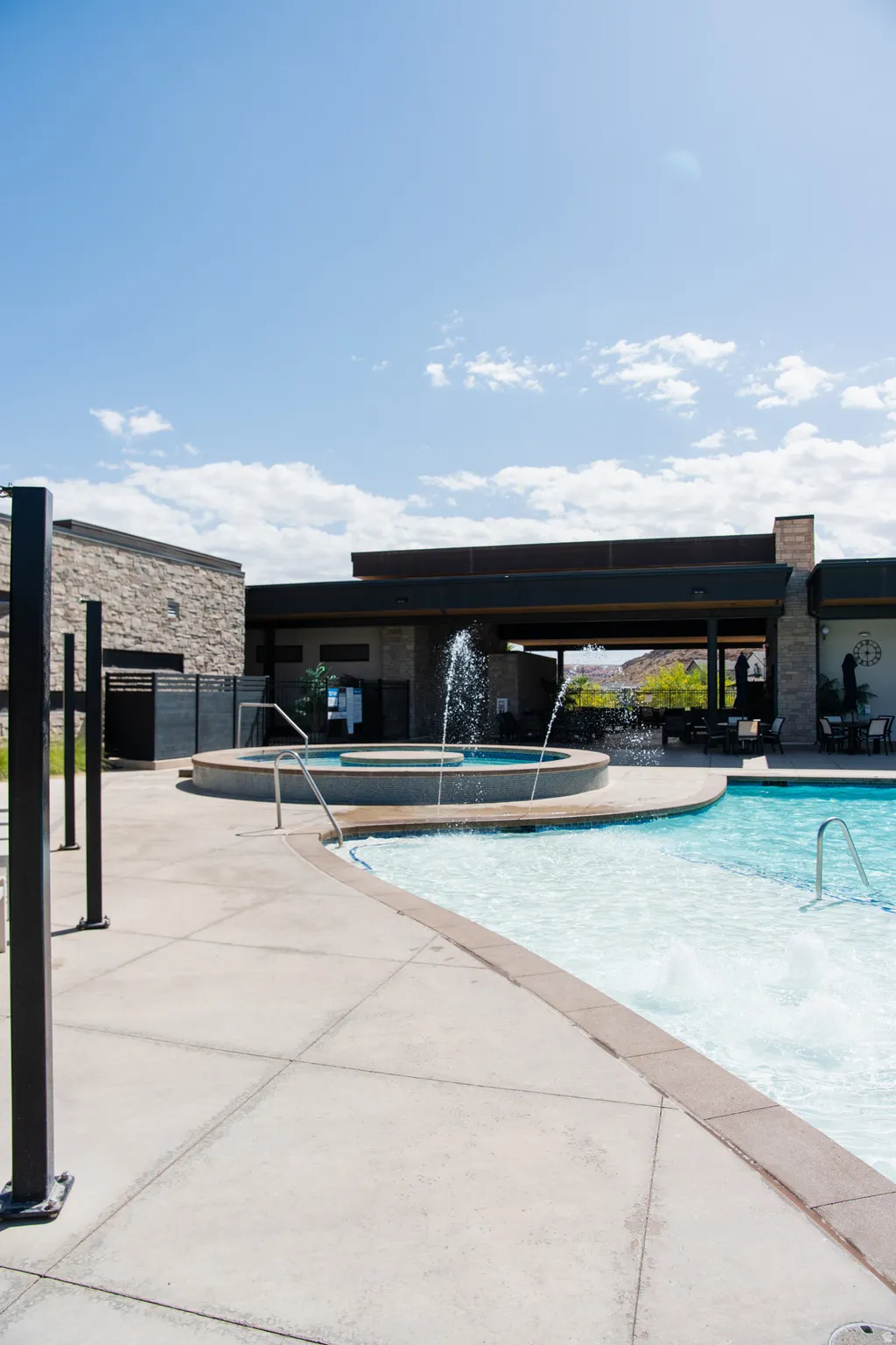 Outdoor pool area featuring a curved swimming pool, an elevated spa with a water feature, and a concrete deck