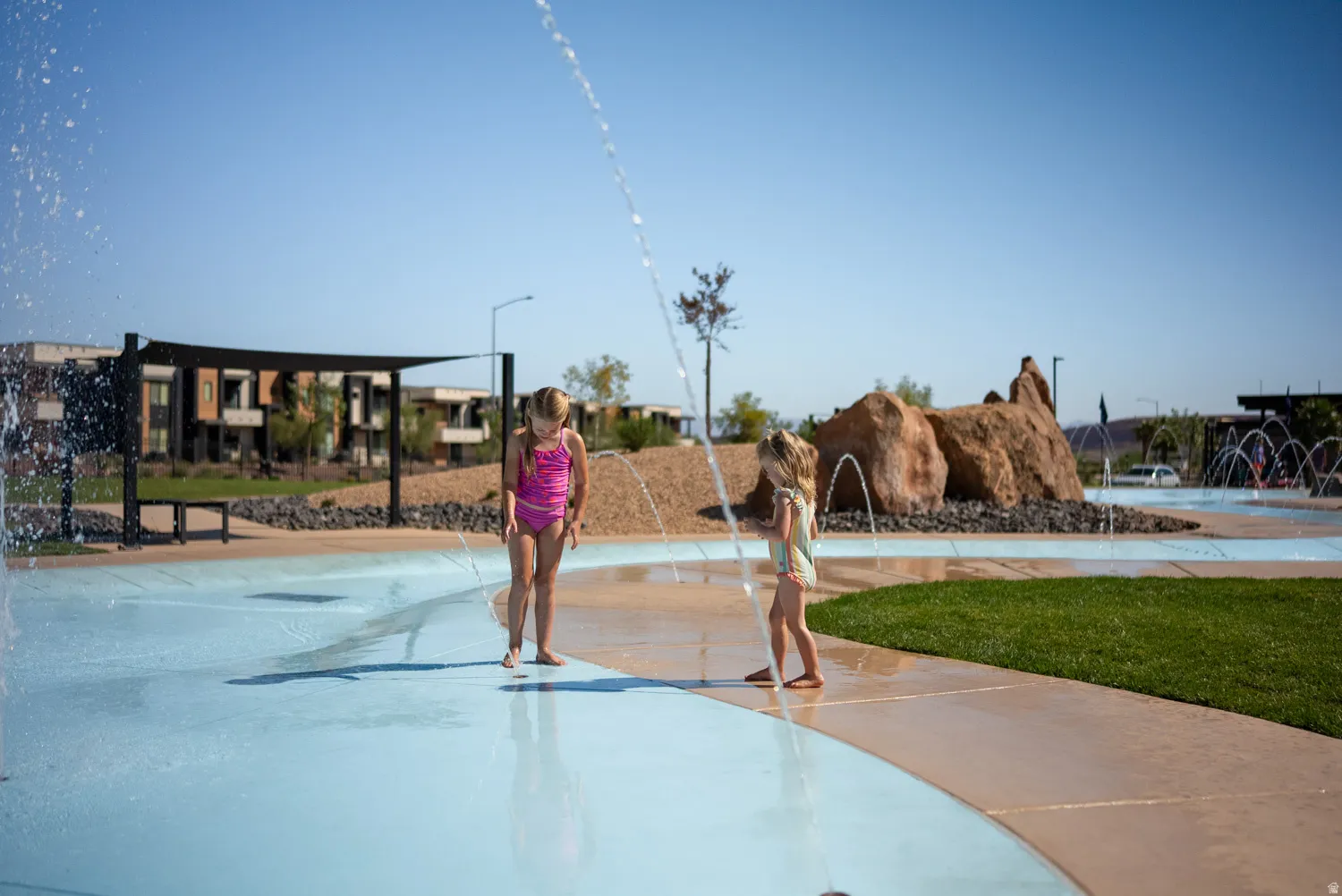 Splash pad and recreational water feature with integrated shallow pool and spray jets, surrounded by manicured lawn and modern hardscape
