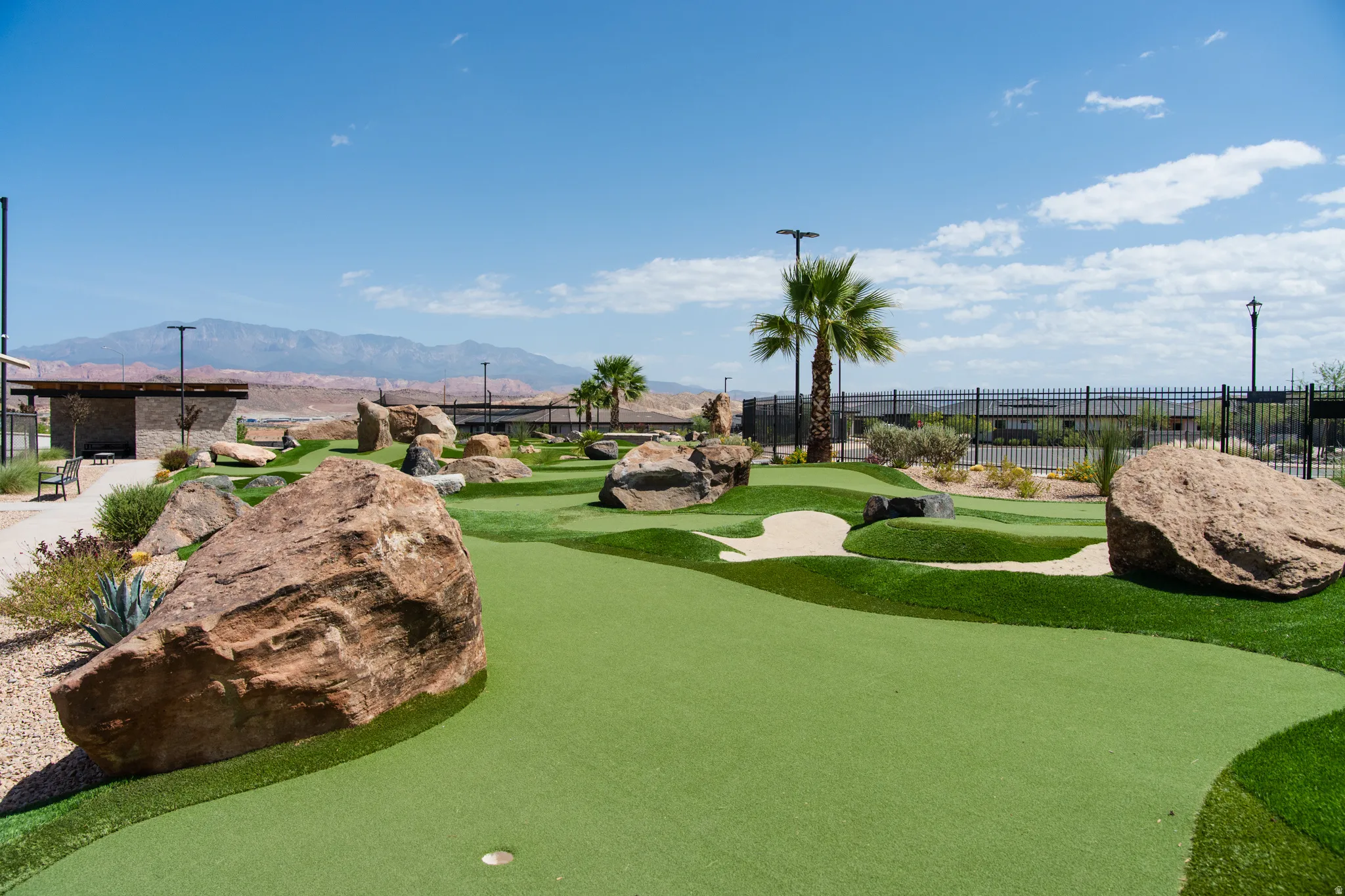 Miniature golf course featuring artificial turf, sand traps, natural rock elements, and palm trees