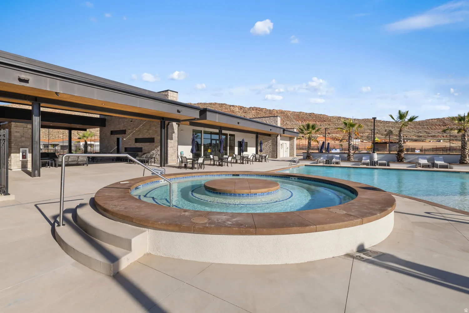 Resort-style outdoor living space featuring a circular tiered spa with integrated seating, expansive saltwater-style pool, and modern pavilion structure with lounge seating