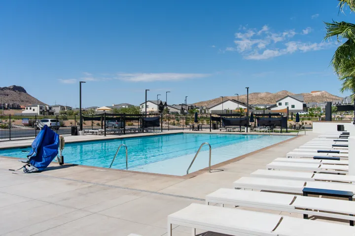 Community swimming pool with surrounding concrete decking, multiple lounge chairs, and shaded seating areas