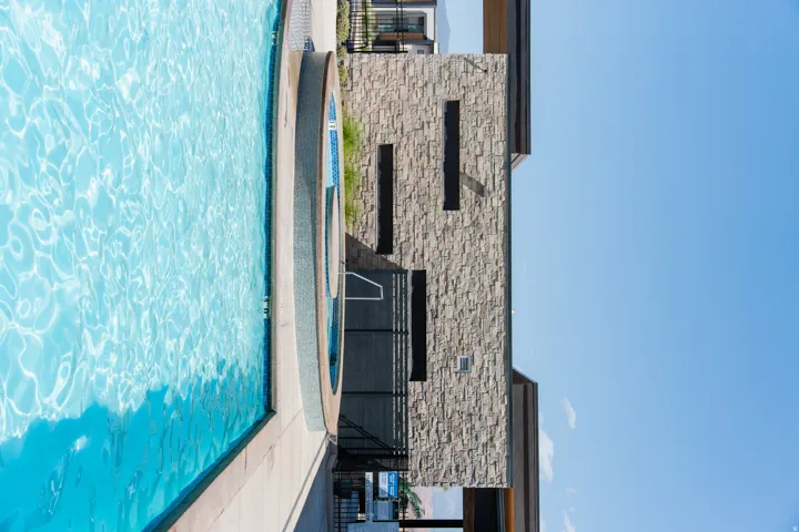 Resort-style swimming pool with an integrated spa, complemented by a stone-clad building featuring modern architectural elements and privacy screening