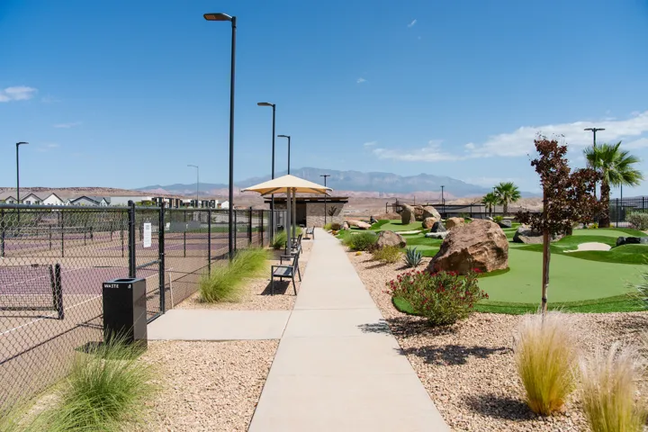 Outdoor recreation area featuring a paved walkway, tennis courts, a putting green, and desert landscaping