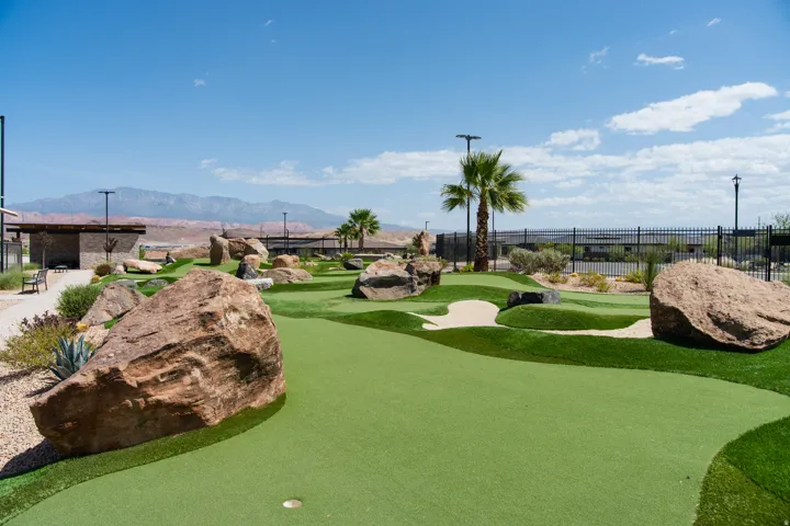Miniature golf course featuring artificial turf, sand traps, natural rock elements, and palm trees