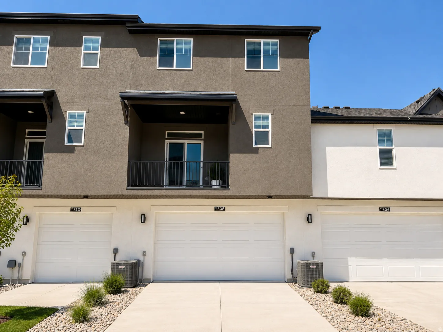 Contemporary stucco exterior featuring a private balcony with black metal railing, white frame windows, and an attached two-car garage with concrete driveway
