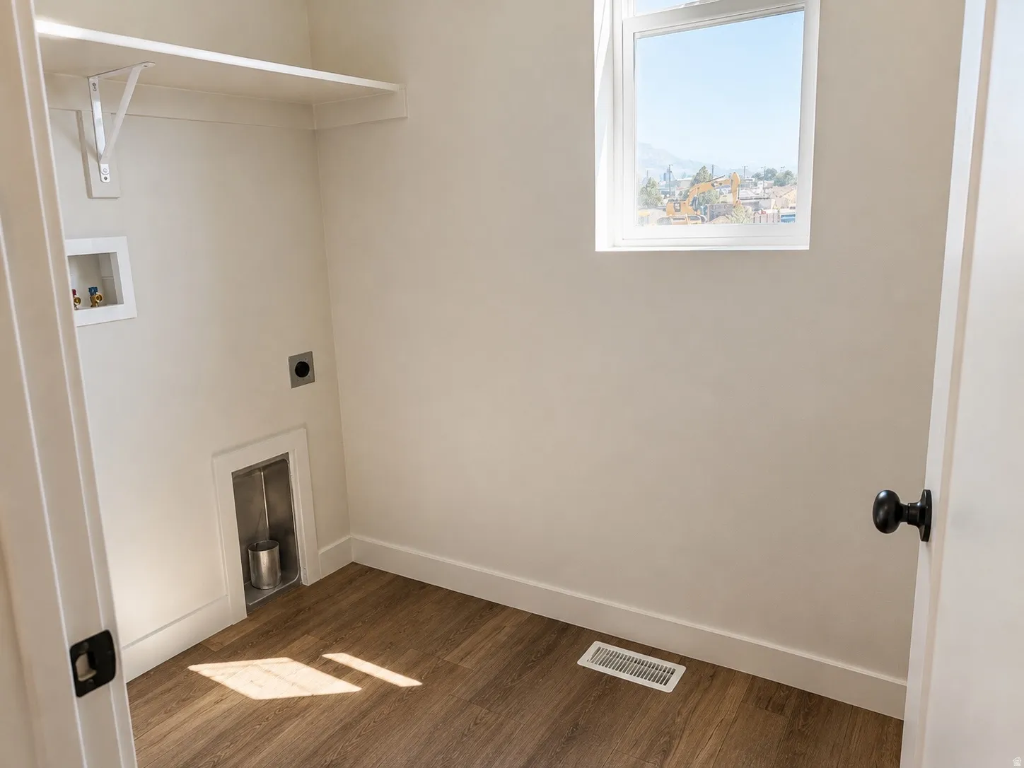 Dedicated laundry space featuring wood-finish flooring, white baseboards, and a single window